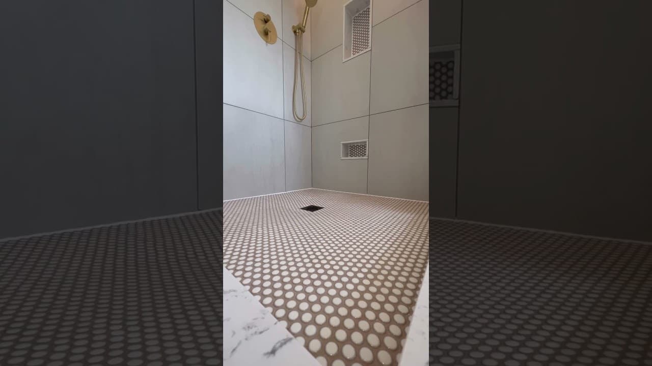 Walk in shower in large format grey tile with brushed gold fittings, two recessed niches and a penny round mosaic floor