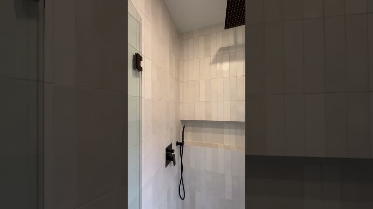 Shower in white vertical stacked tile with a matte black rainfall head, handheld and a built in ledge