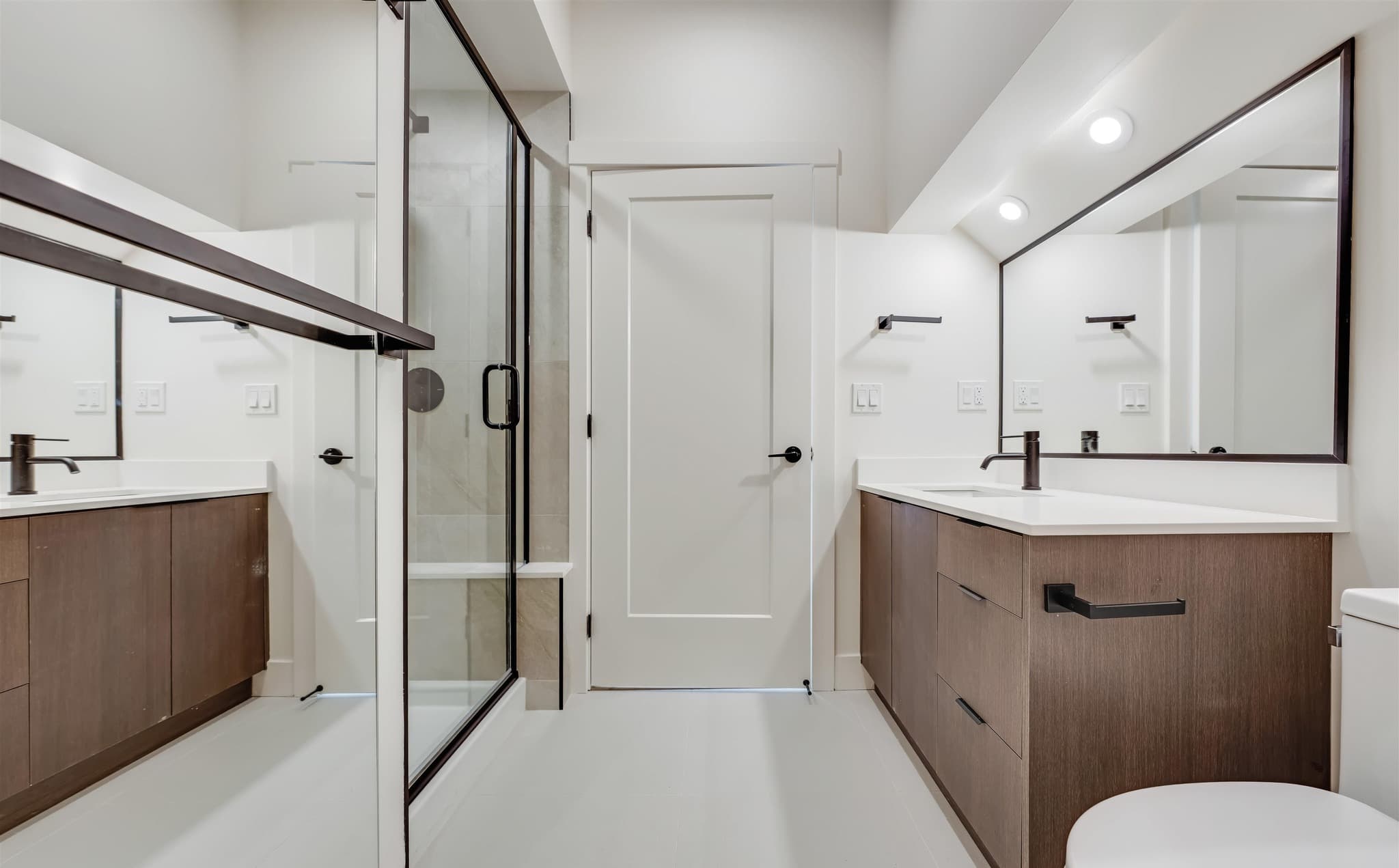 Condo ensuite with twin dark wood vanities, black framed mirrors and a glass shower