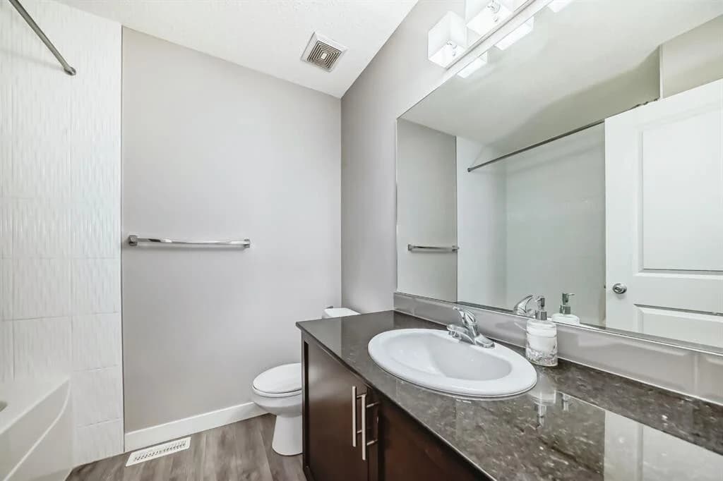 Condo bathroom with a dark wood vanity, granite top and a tub and shower surround