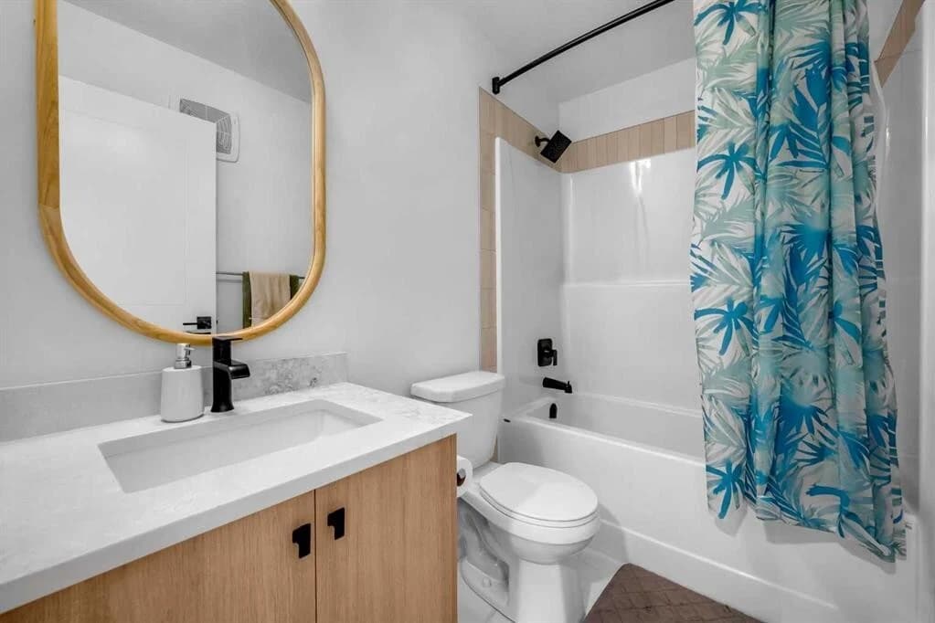 Condo bathroom with a light oak vanity, round timber framed mirror and a tub and shower surround