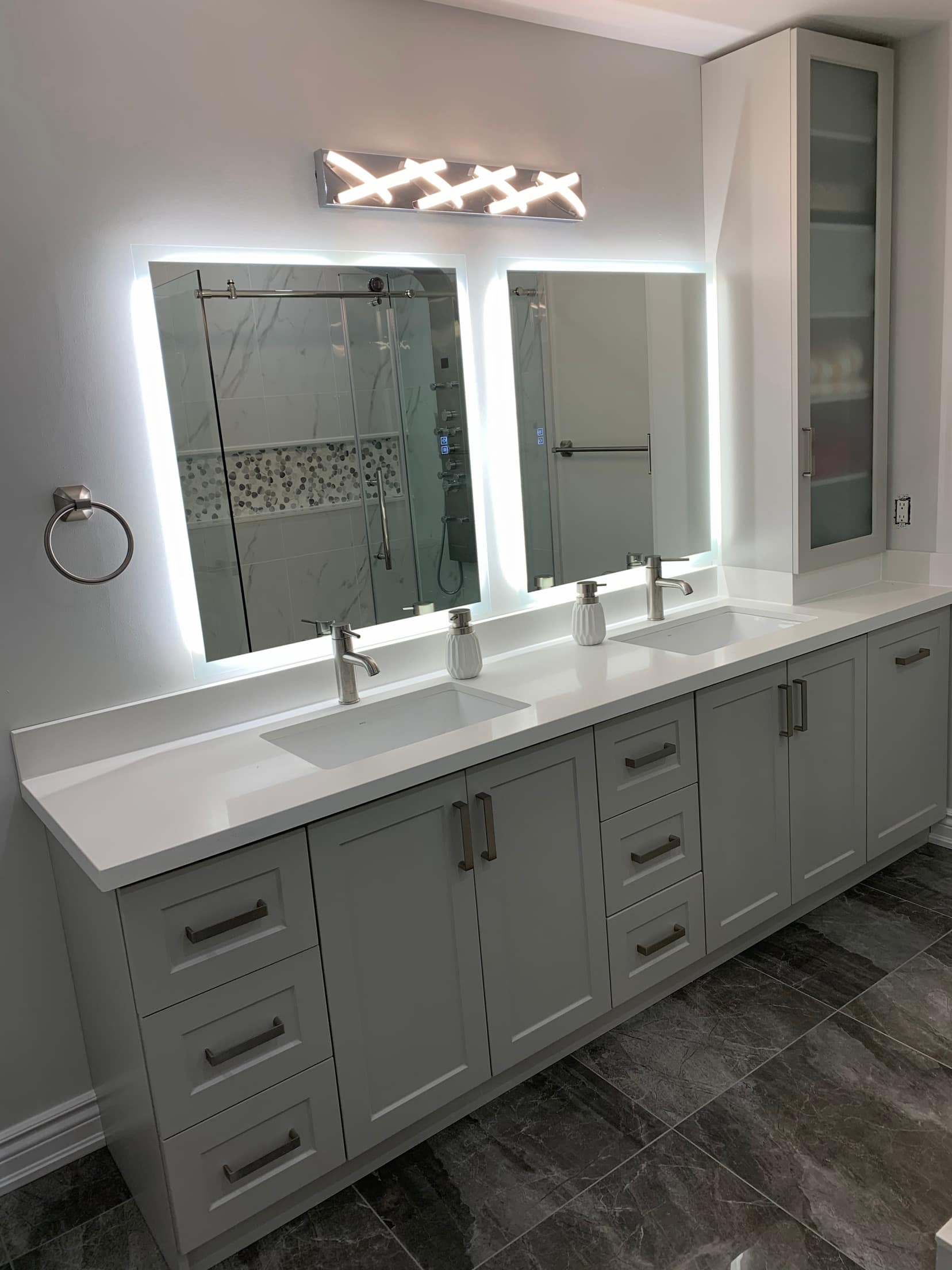 Long grey double vanity with twin backlit mirrors and a glass fronted linen tower