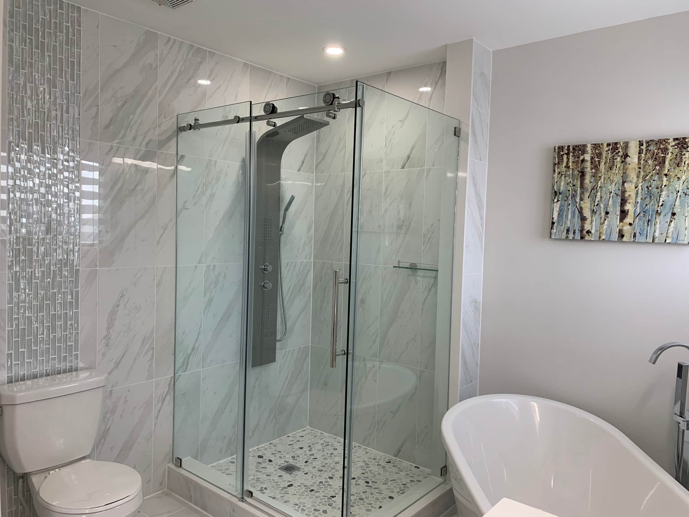 Corner glass shower with a mosaic feature strip and pebble floor, next to a freestanding tub