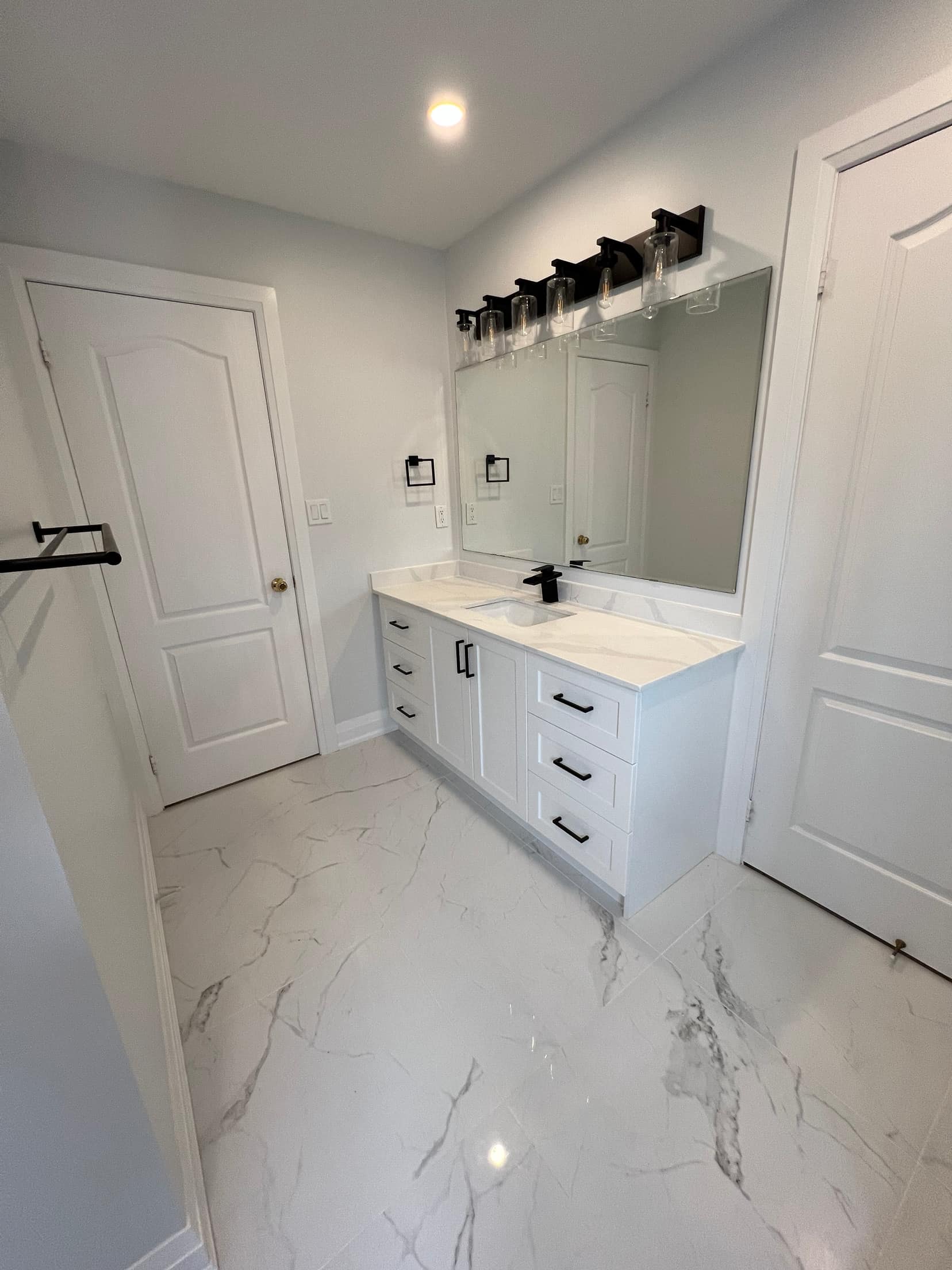 White shaker vanity with black hardware and lighting on large format marble look floor tile