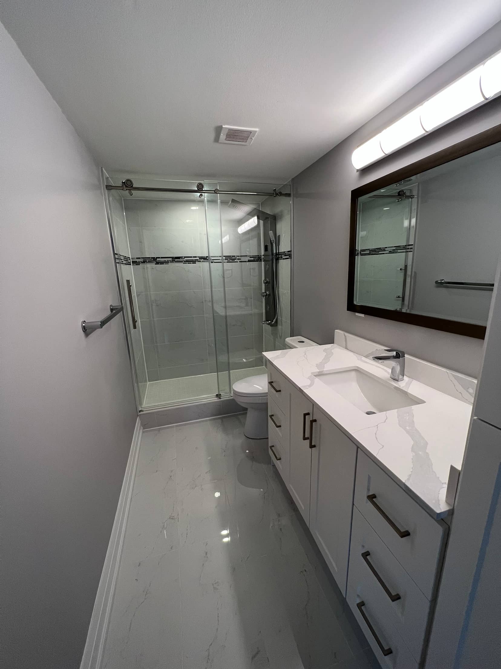 Sliding glass shower with a mosaic accent band, beside a white vanity and framed mirror