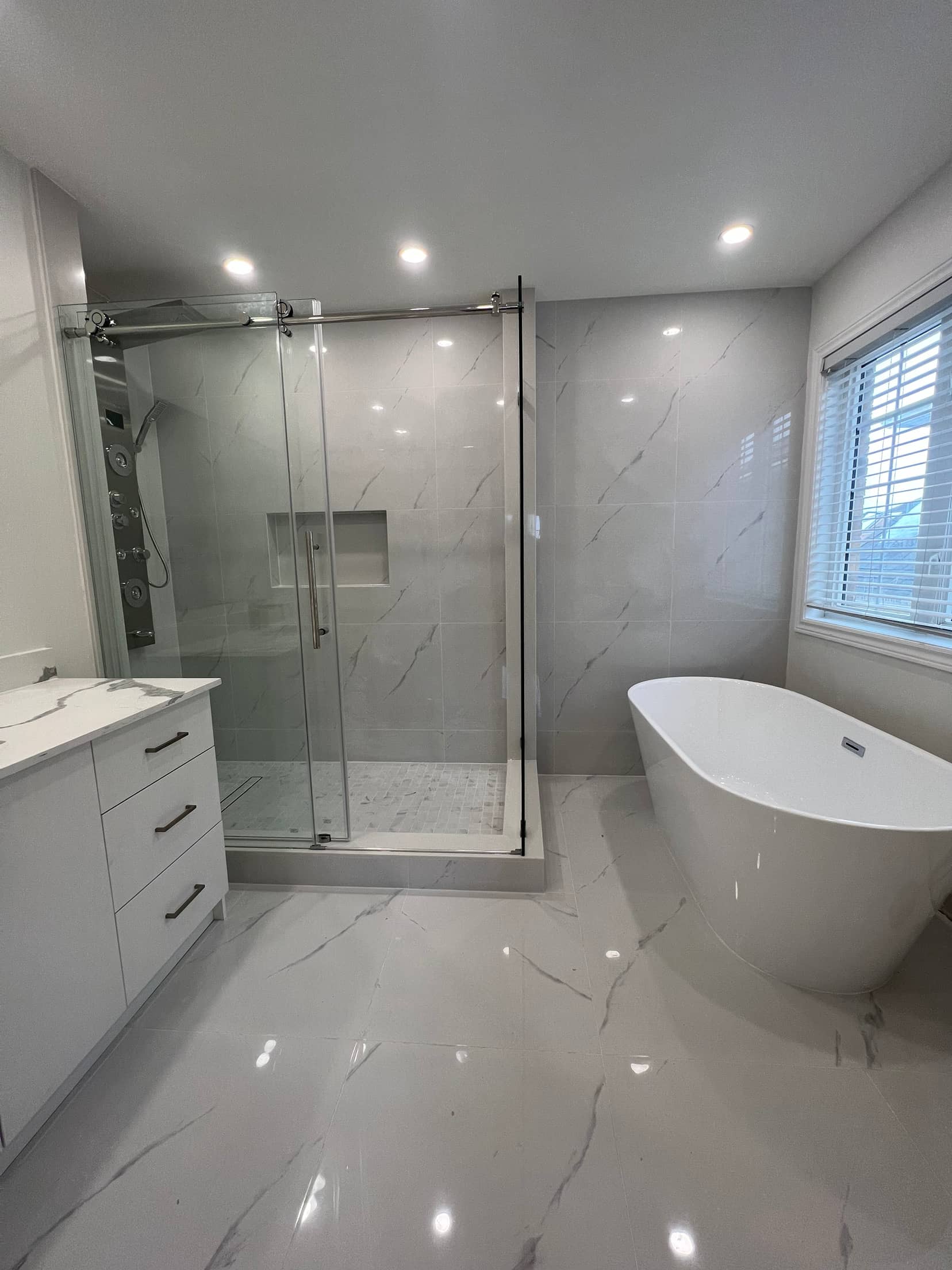 Sliding glass shower with a stainless panel and recessed niche, a freestanding tub by the window and a white vanity
