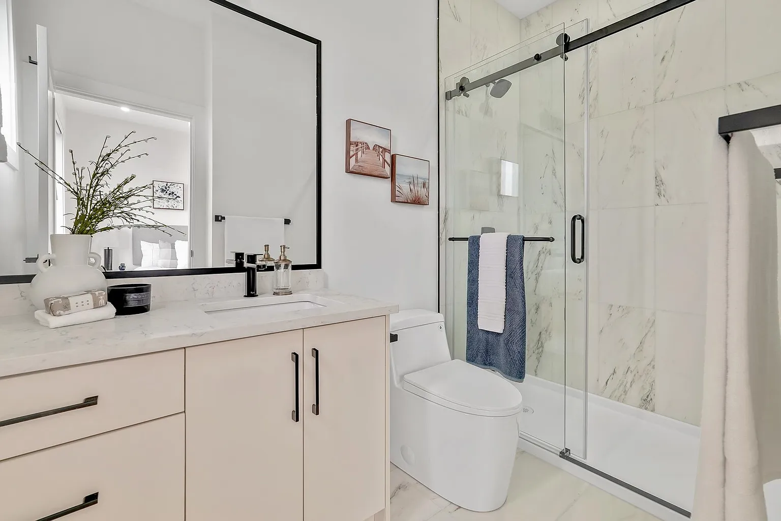 Condo bathroom with a pale wood vanity, black framed mirror and hardware, and a marble tiled shower behind sliding glass