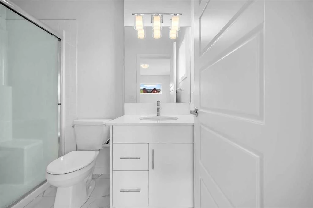 Compact all white condo bathroom with a single vanity, tub and shower behind sliding glass, and marble look floor tile