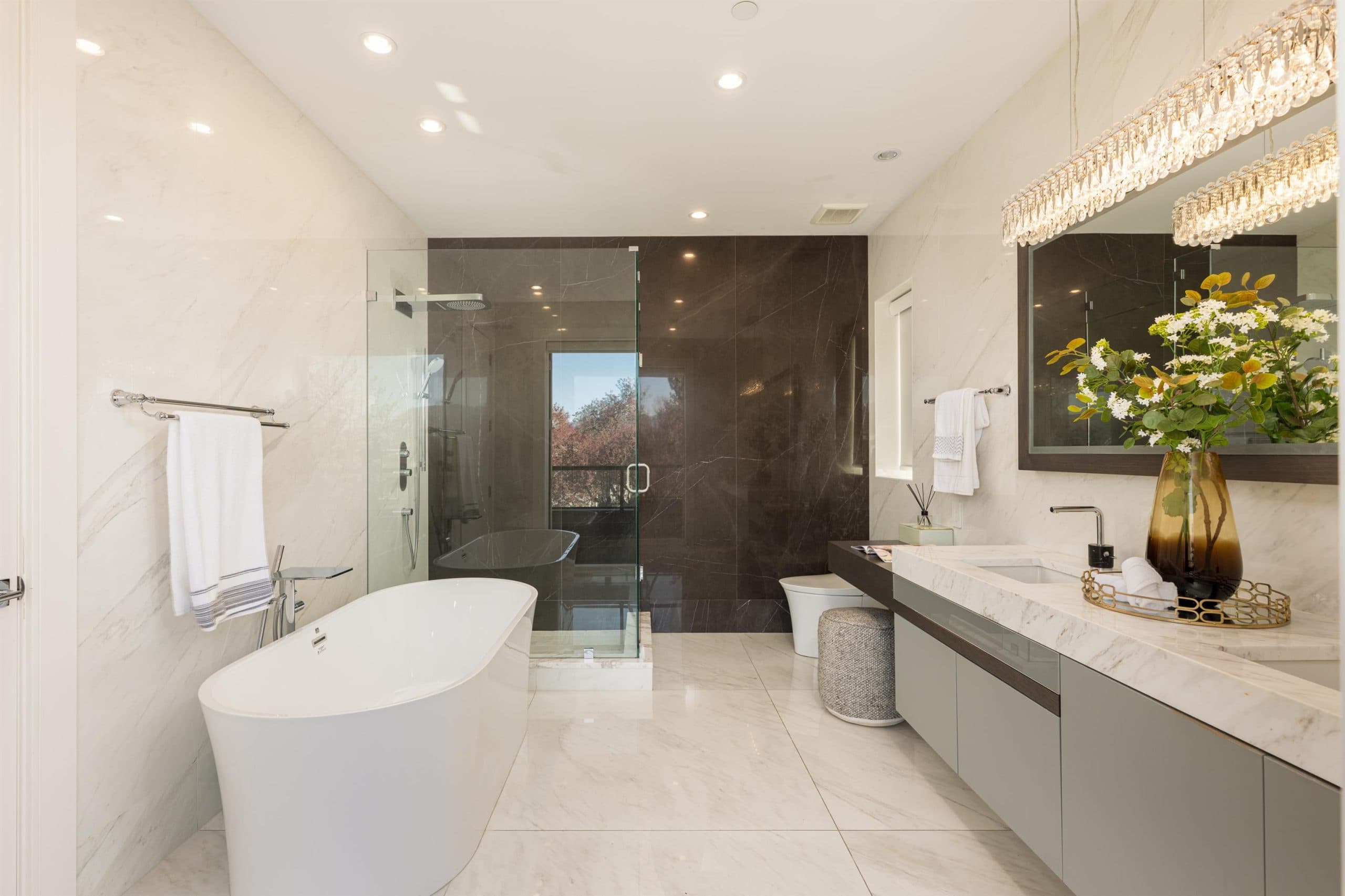 Marble ensuite with a freestanding tub, walk in shower behind a dark marble wall and a crystal light bar over the vanity