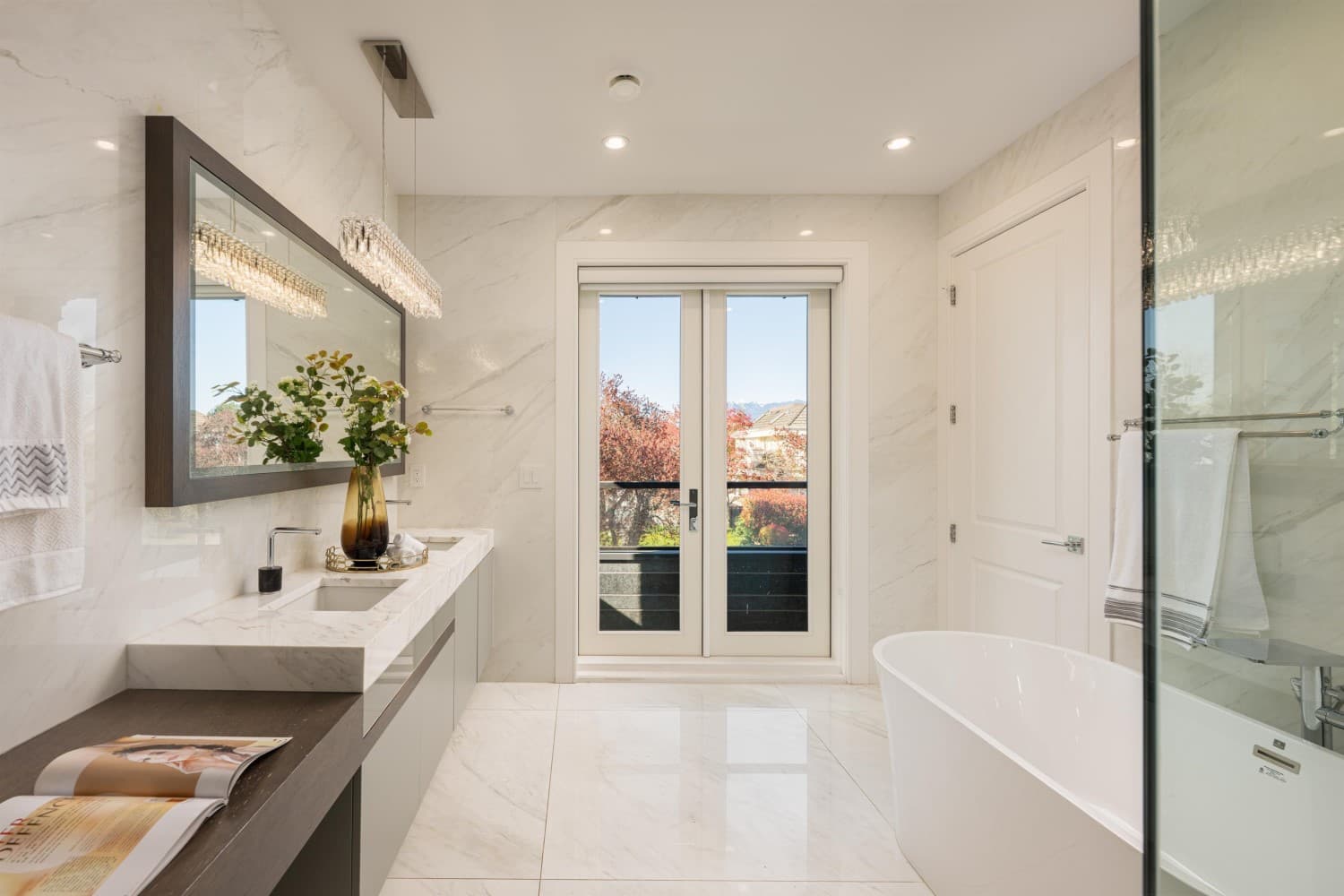 Marble clad ensuite with a floating vanity, crystal linear pendant, freestanding tub and French doors to a balcony