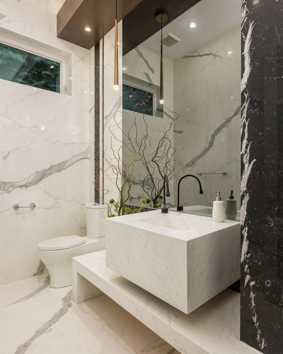 Powder room with a solid marble block basin, book matched marble walls and brass pendants